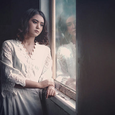Woman looking out window with sad expression.